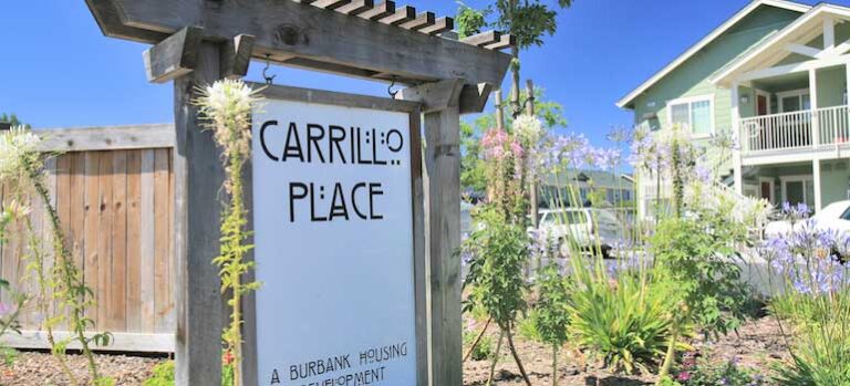 Sign reading "Carrillo Place" with a garden in the foreground and a residential building in the background.